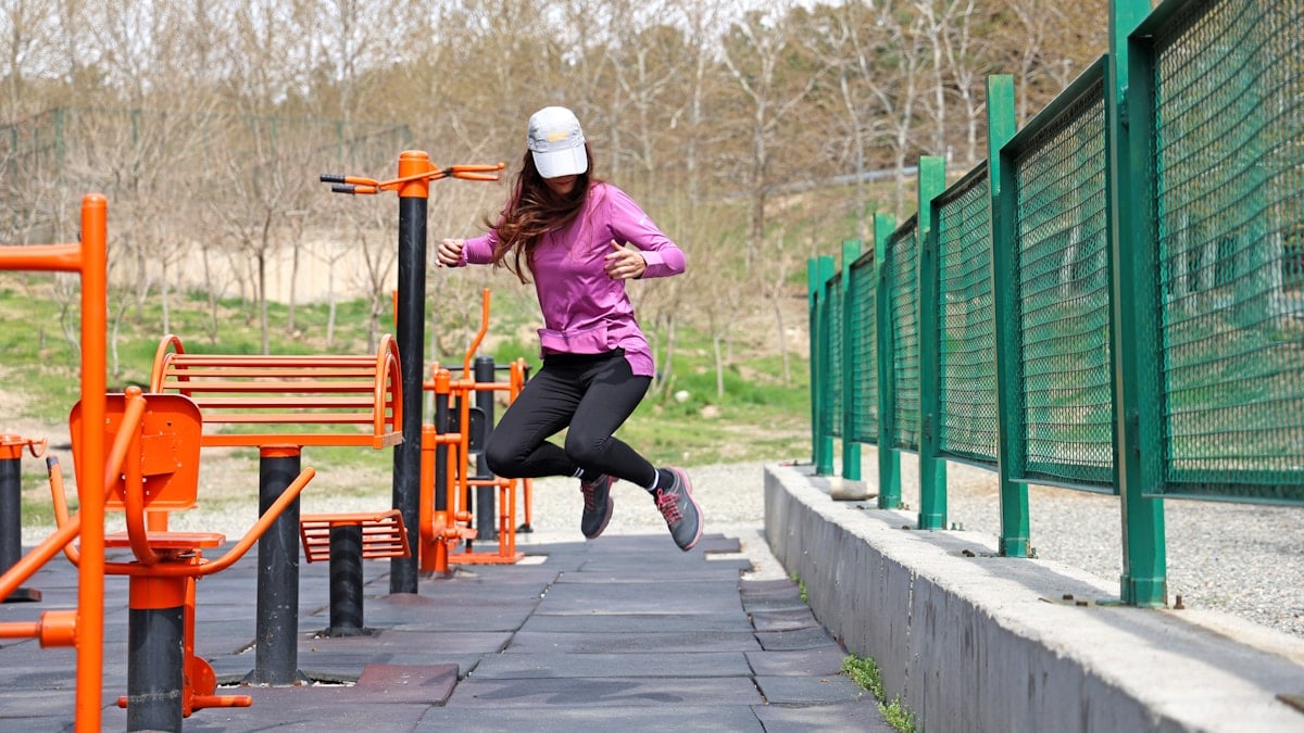 A young female model wearing sportswear is jumping in the air at a park's sports area. The photo is captured with a high shutter speed.